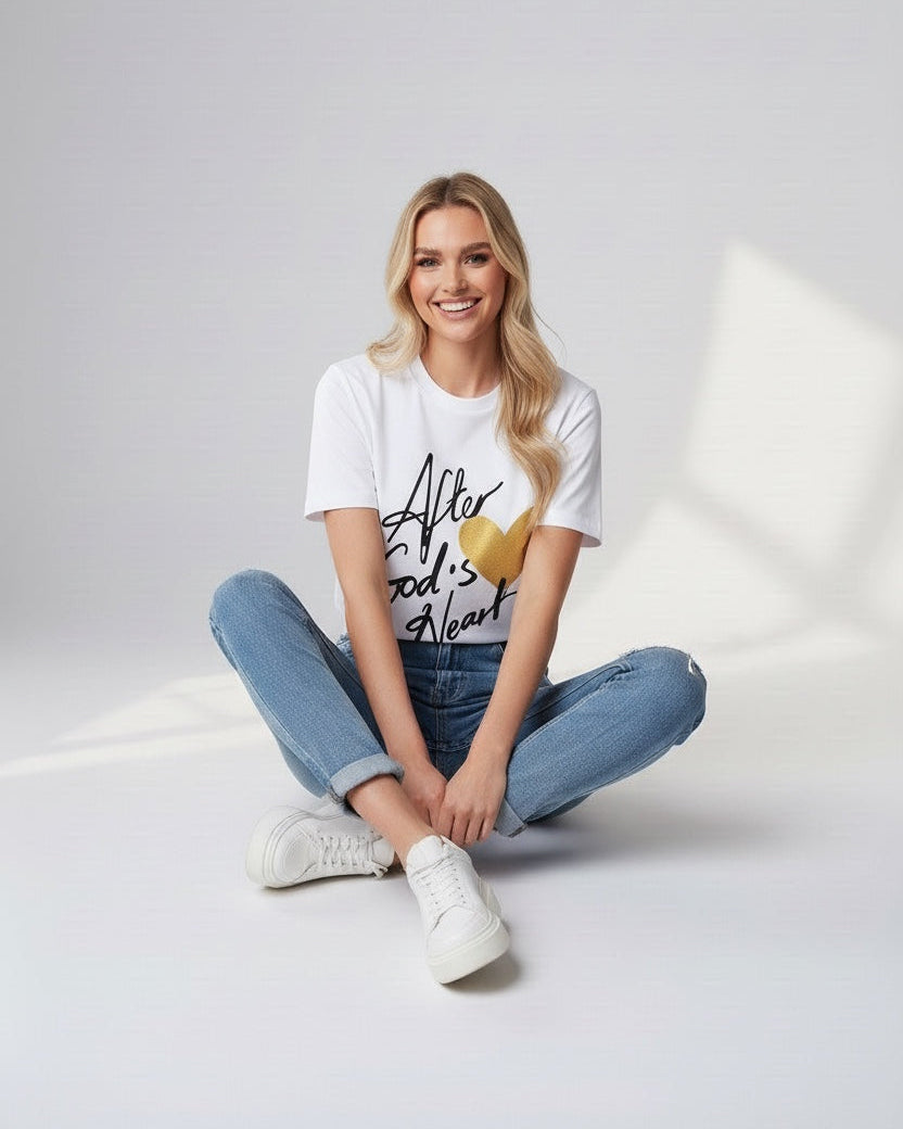 Woman sitting on a light gray floor wearing a white t-shirt with text and blue jeans.