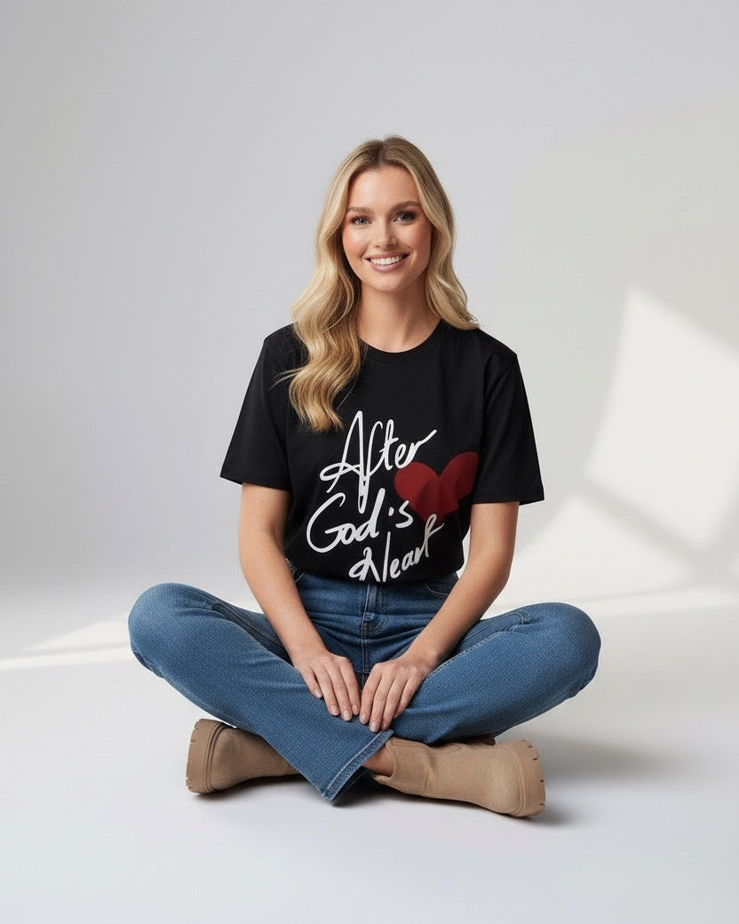 Woman wearing a black t-shirt with text and a heart design, sitting on a white floor.
