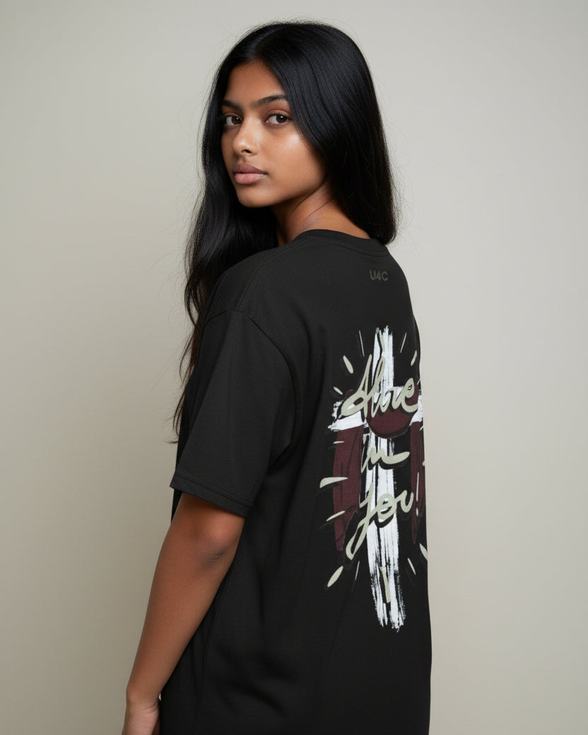 Person wearing a christian black t-shirt with a graphic design on the back, standing against a plain background.