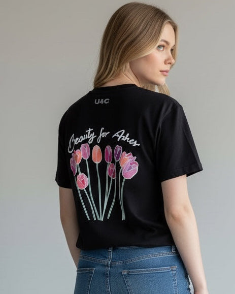 Woman wearing a black t-shirt with floral design and text, paired with blue jeans on a plain background