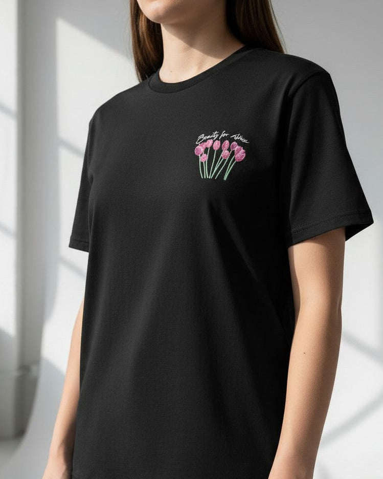 Person wearing a black christian  t-shirt with pink tulip design in a bright room. Beauty for ashes 