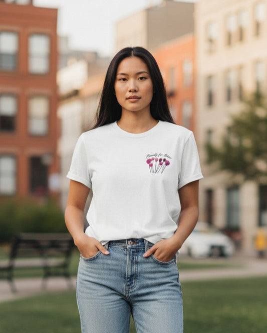 Person wearing a white t-shirt with a graphic design and light blue jeans, standing on a sidewalk with buildings in the background.Beauty for Ashes pocket white t-shirt 