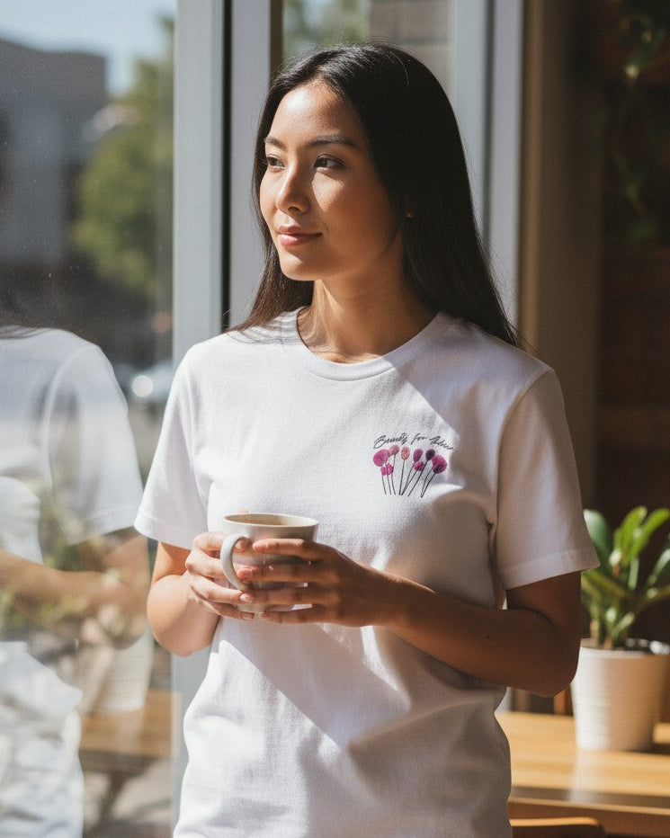 Woman in a white t-shirt holding a coffee cup in a cafe. Beauty for Ashes pocket white t-shirt 