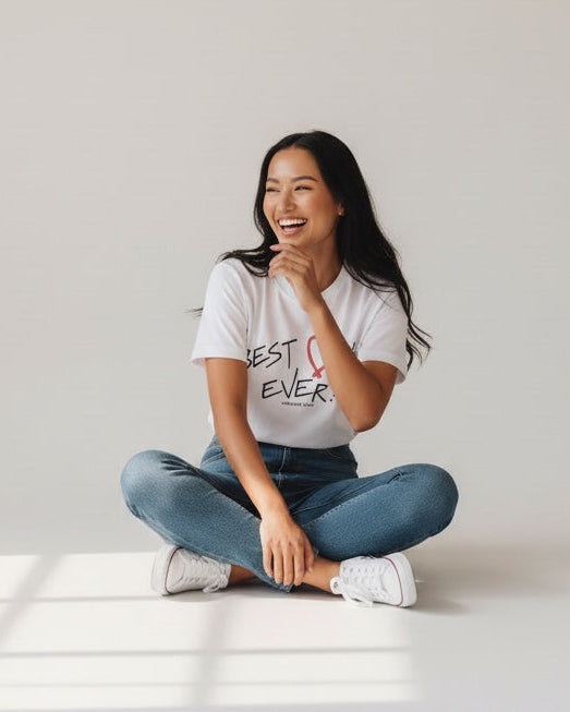 Woman sitting on the floor with a 'Best Ever' t-shirt in a bright room.