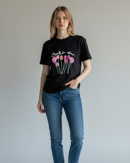 Woman wearing a black t-shirt with a floral design and text, standing against a plain background, beauty for ashes 