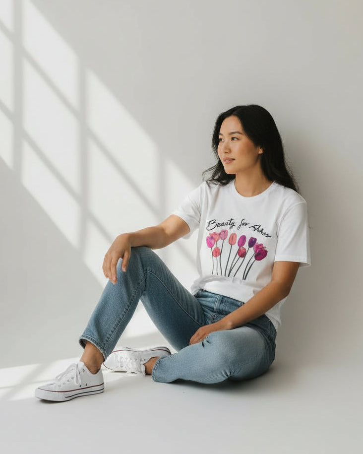 Woman sitting on a white floor wearing a christian white t-shirt with a floral design and text.