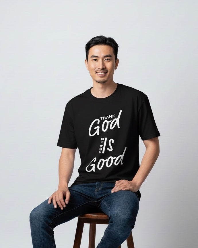 Man sitting on a stool wearing a black t-shirt with text, on a plain background