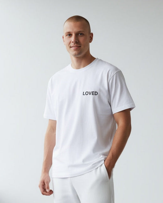 Person wearing a white t-shirt with 'LOVED' text in a minimalistic room.