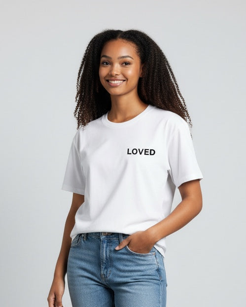 Woman wearing a white t-shirt with 'LOVED' text, blue jeans, and white sneakers on a plain background