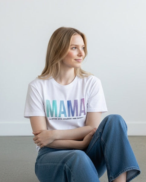 Woman sitting on the floor wearing a white t-shirt with colorful text and blue jeans.