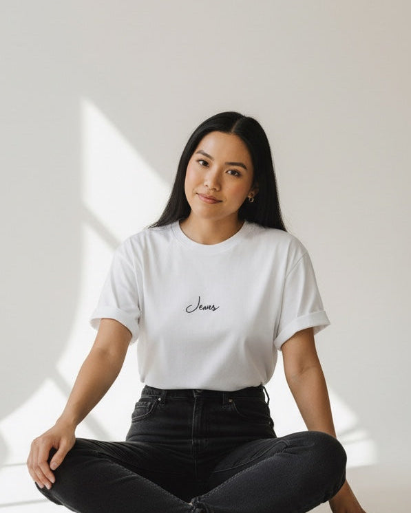 Woman sitting on the floor wearing a white t-shirt and black pants in a minimalistic setting.