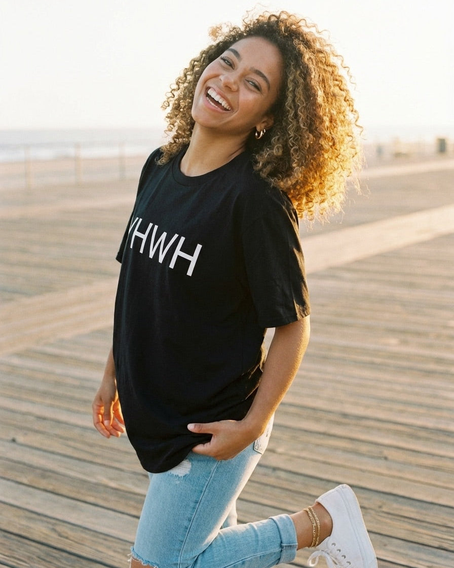 Woman wearing a black t-shirt with 'KWH' on it, standing on a wooden boardwalk.