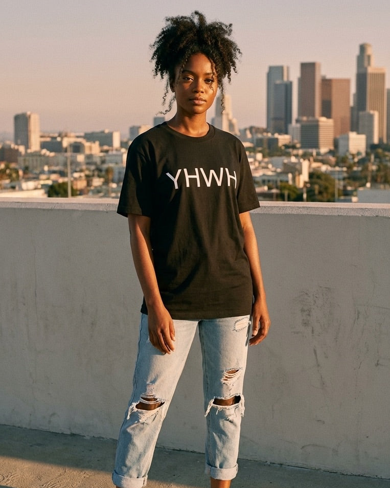Person wearing a black t-shirt with 'YHWH' text on a rooftop with city skyline in the background