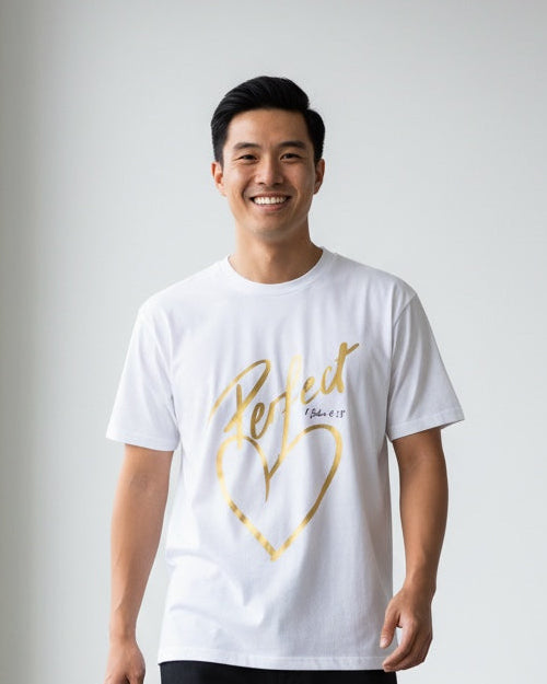 Man wearing a white t-shirt with gold text and black pants standing in a minimalistic room.