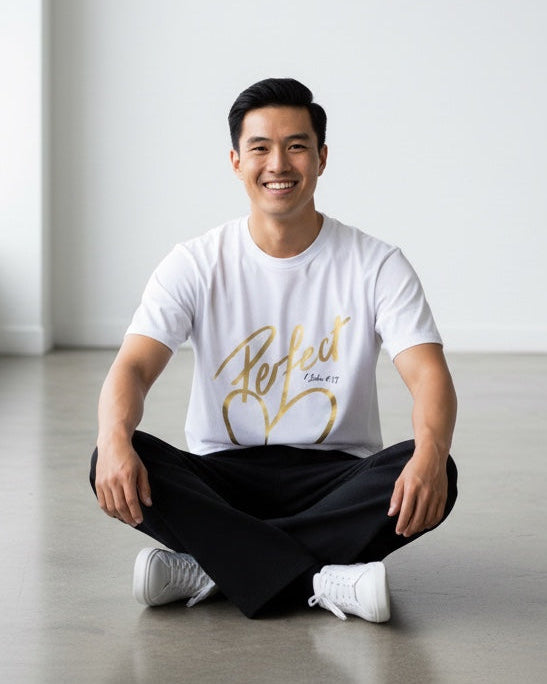 Man sitting on the floor in a minimalistic room wearing a white t-shirt with gold text.